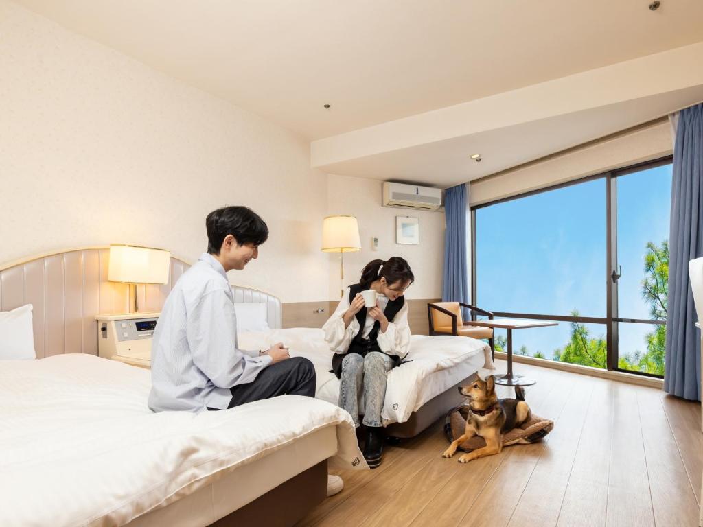 a couple in a hotel room with a dog sitting between beds at Wan Wan Paradise Izukogen in Ito