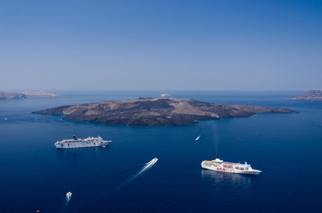 tres barcos en un gran cuerpo de agua con una isla en Morfes Luxury Suites by Caldera Houses, en Firostefani