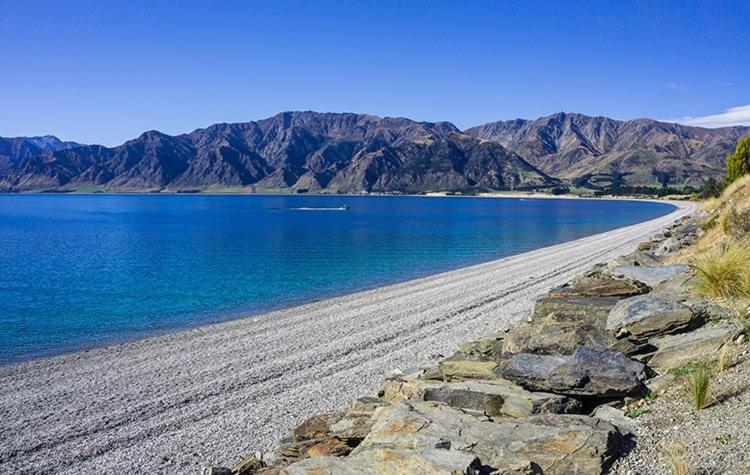 a beach with blue water and mountains in the background at The Bothy by the lake in Lake Hāwea