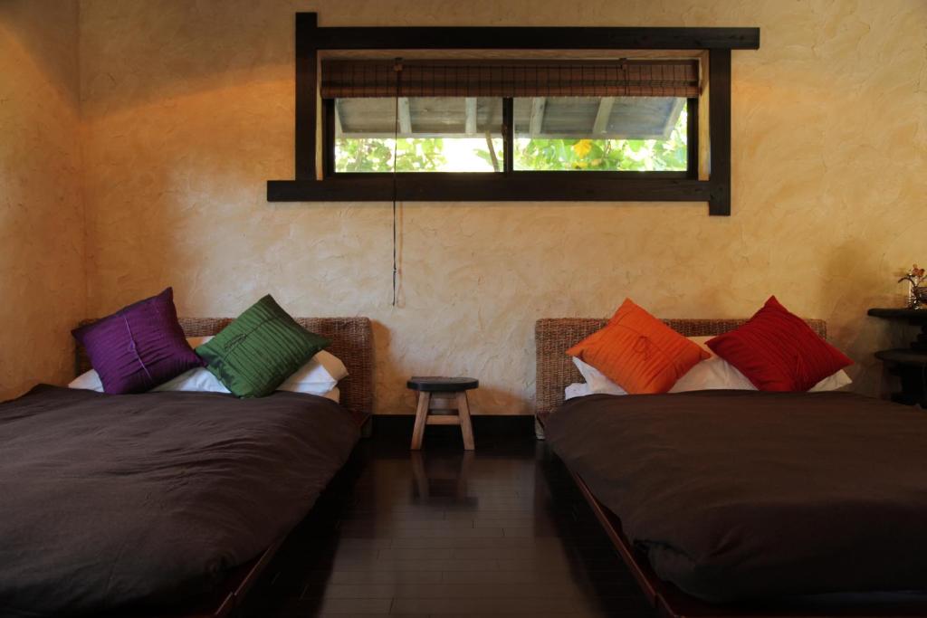 two beds with colorful pillows in a room with a window at Taketomijima Akaneya in Taketomi