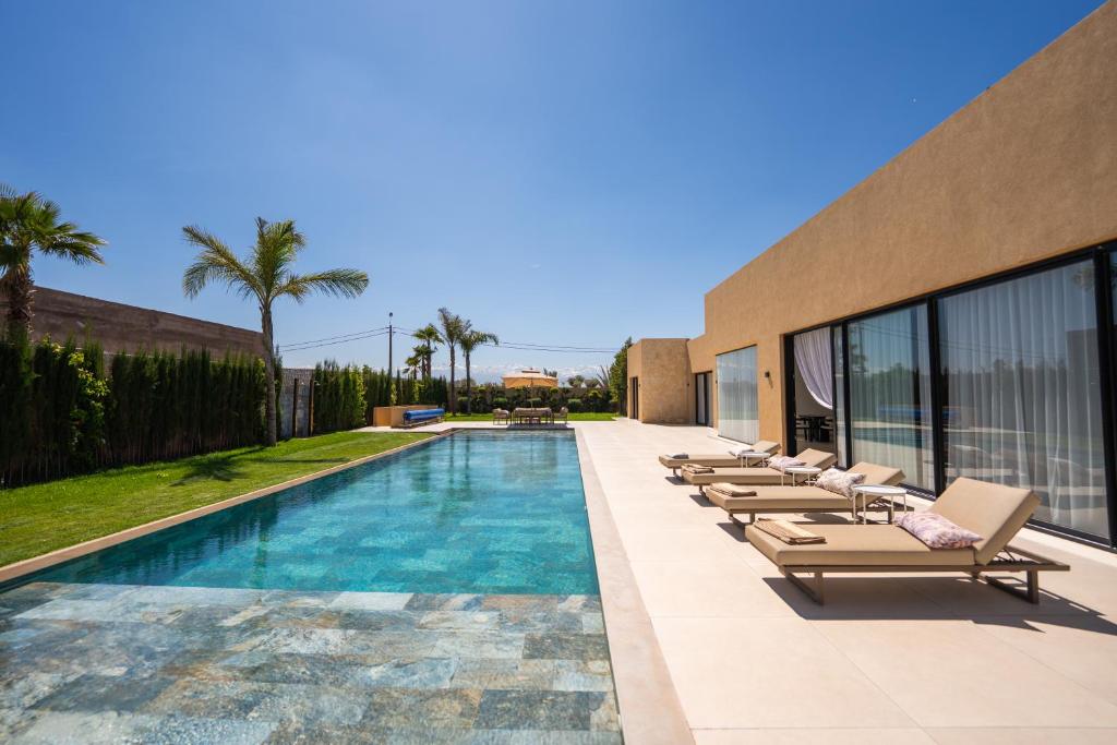 a swimming pool with lounge chairs next to a building at Villa prestige, terrain padel, salle de sport, hammam in Aït Amara el Ouled