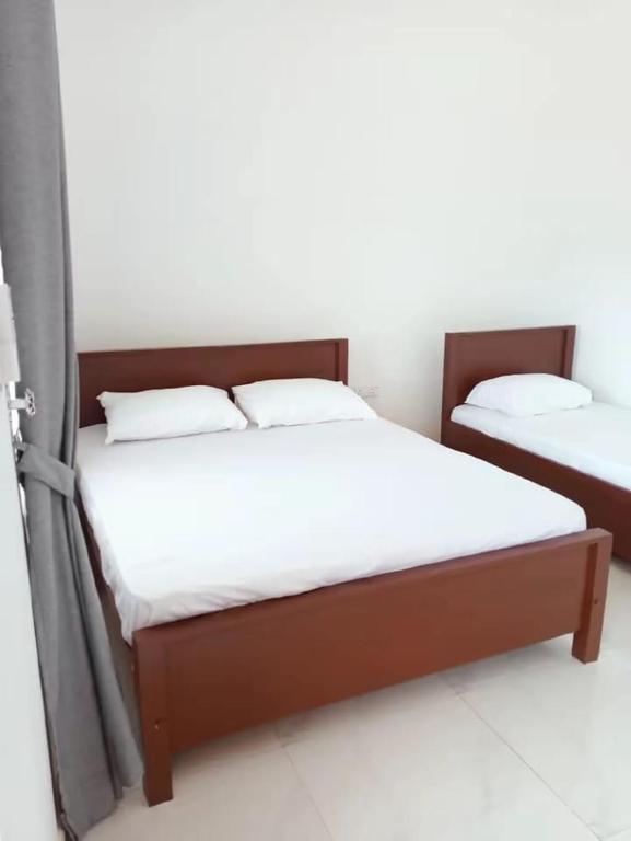 two beds in a room with white sheets and pillows at Mano Holiday Guest House in Kalkudah