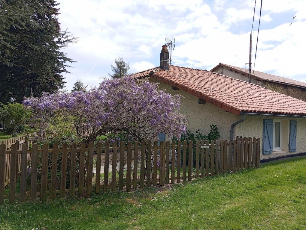a fence in front of a house with a purple tree at Le soleil in Chabanais