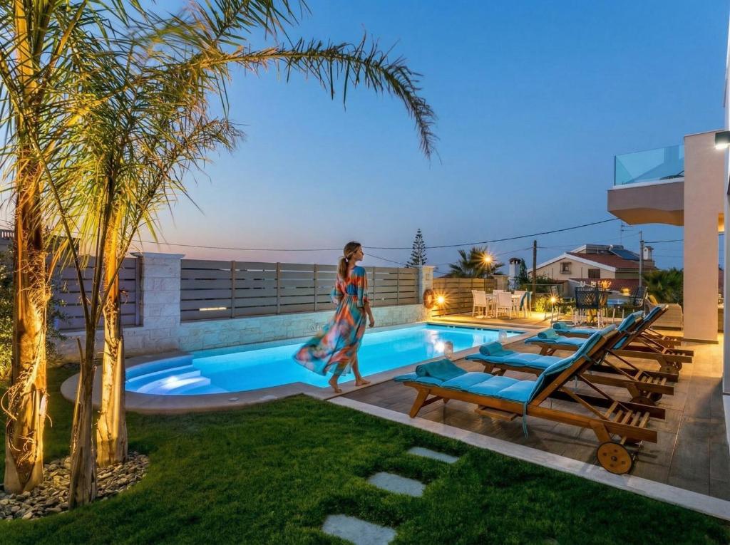 a woman walking by a swimming pool at night at SUPERIOR VILLA MARINA MARE Sauna - Hammam - Pool - 250m from Beach in Agia Marina Nea Kydonias