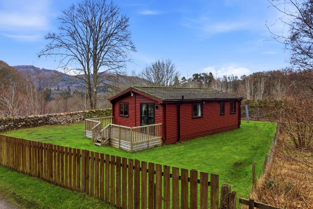 a small red cabin with a fence in the grass at Braeknowe Scottish Cabin Getaway in Dunkeld