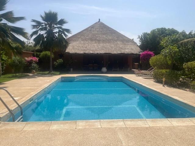 a swimming pool in front of a house with a thatch roof at Superbe villa avec piscine privée à 500m de la plage à Nianing in Nianing