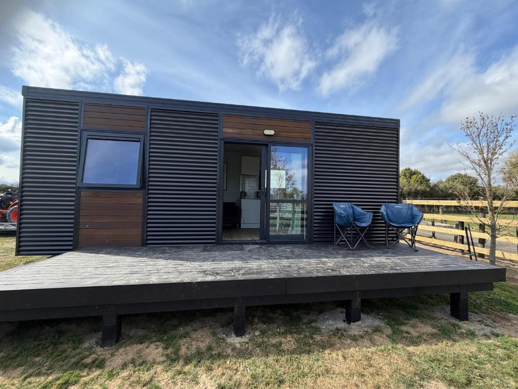 a black tiny house with two chairs on a deck at Benrose Stables Cottage in Palmerston North