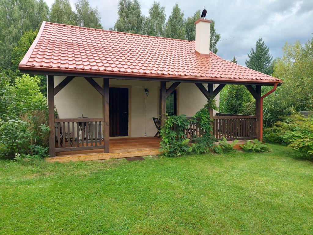 a small house with a wooden deck in a yard at Domek nad jeziorem, łódka, kajak in Zalewo