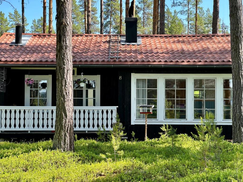 a black house with a red roof and trees at Sunshine Stuga Mörtsjön in Stugun