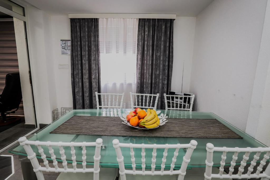 a bowl of fruit on a glass table with chairs at Apartman Lena lux in Vrnjačka Banja
