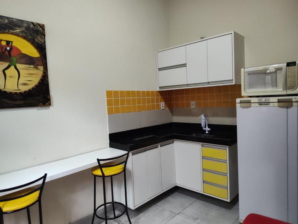 a small kitchen with white cabinets and yellow bar stools at Funcional, cômoda e confortável in Camaçari