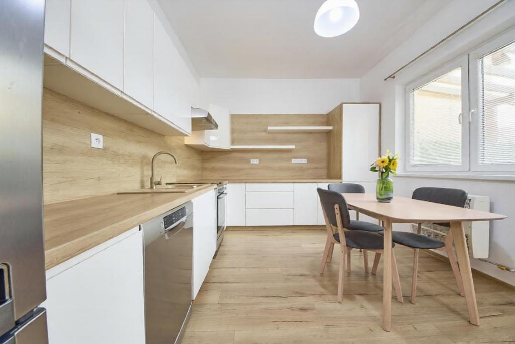 a kitchen with white cabinets and a wooden table and chairs at Danubia Apartment Gabčíkovo in Gabčíkovo
