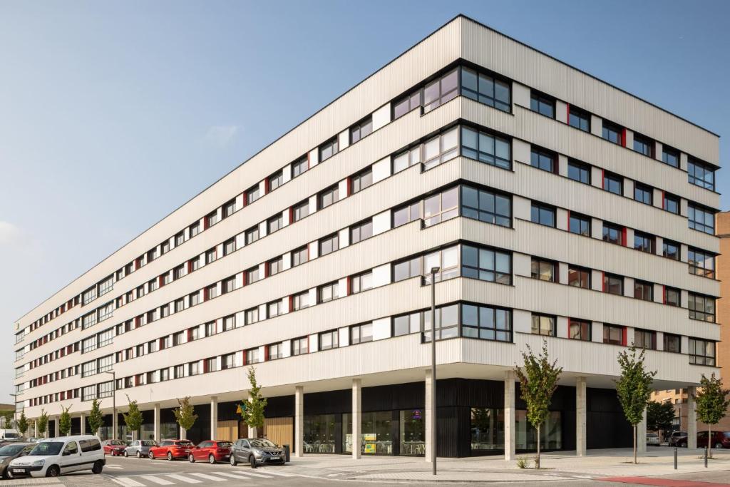 a large white building with cars parked in a parking lot at Amro Pamplona - Albergue Juvenil in Pamplona
