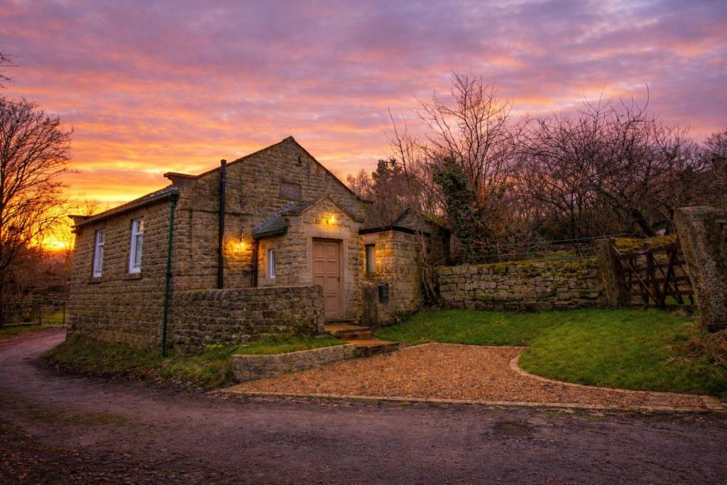 an old stone house with a sunset in the background at The Old Chapel, Peak District in Bamford