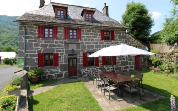 a small stone house with a table and an umbrella at Le relais de Lustrande in Brezons
