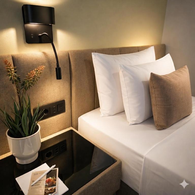 a bed with white pillows and a lamp and a plant at Hotel Turist - City Center in Skopje