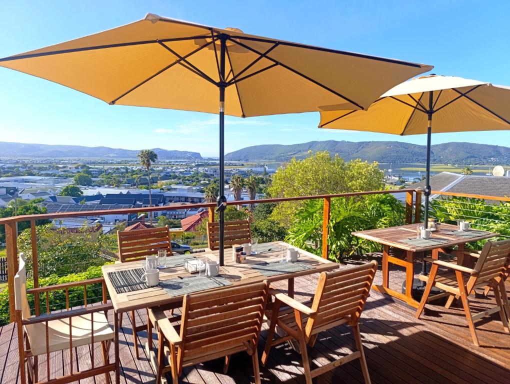 a patio with tables and umbrellas on a deck at Guinea Fowl Lodge - Lagoon & Heads View B&B, Central Knysna in Knysna