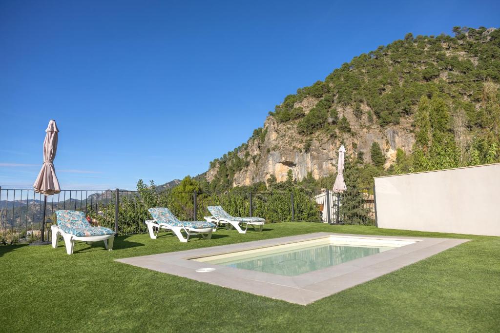 a backyard with a pool and two chairs and an umbrella at Apartamentos 7 puentes sierra Cazorla Los 2 Dúplex in Burunchel