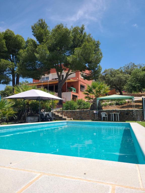 a blue swimming pool with an umbrella and a building at Casa Terra in Hontanar