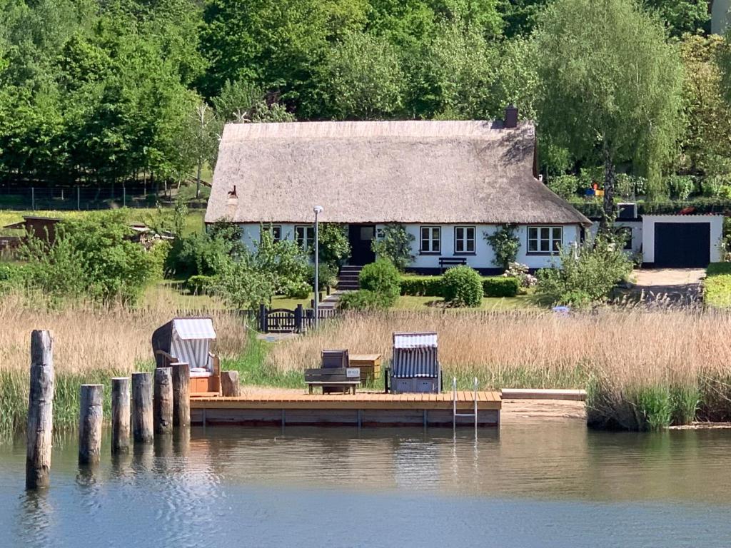 a house with three chairs sitting on a dock next to the water at Seedorf Hideaway, Reethaus mit Garten und Privatsteg, Kamin, Sauna und Hot Tub in Ostseebad Sellin