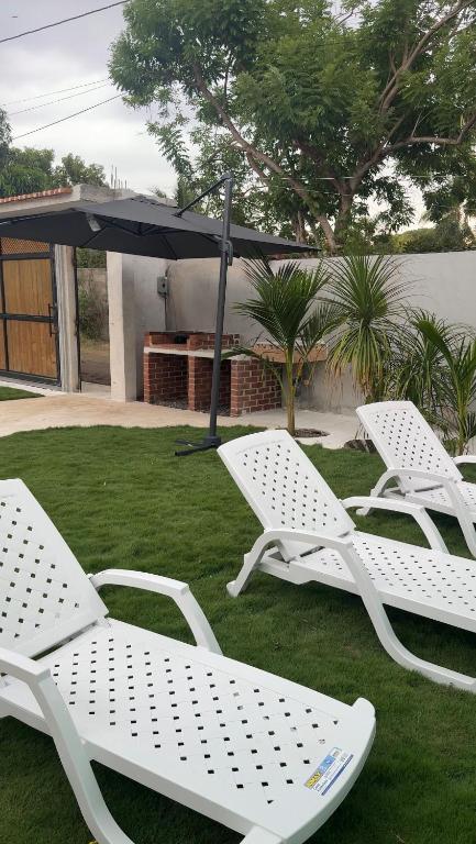 three white lawn chairs and an umbrella on the grass at Monterrico VIP in La Candelaria
