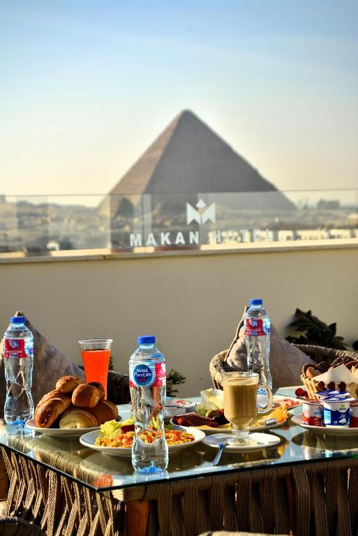 a table topped with plates of food with a pyramid in the background at Makan Pyramids View in Cairo