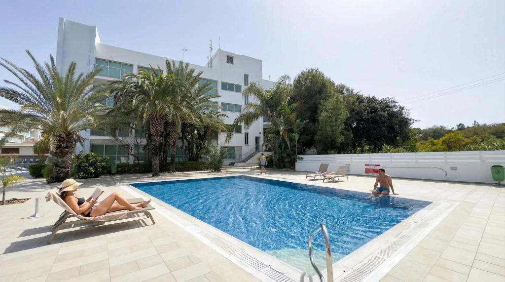 a woman sitting in a chair next to a swimming pool at Coralli Beachfront 1BDR Protaras in Paralimni