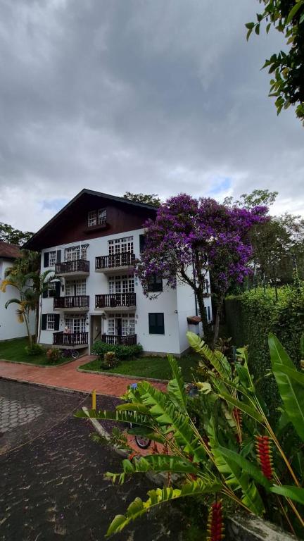 a white building with a tree with purple flowers at duplex aconchegante com varanda em condominio in Nova Friburgo