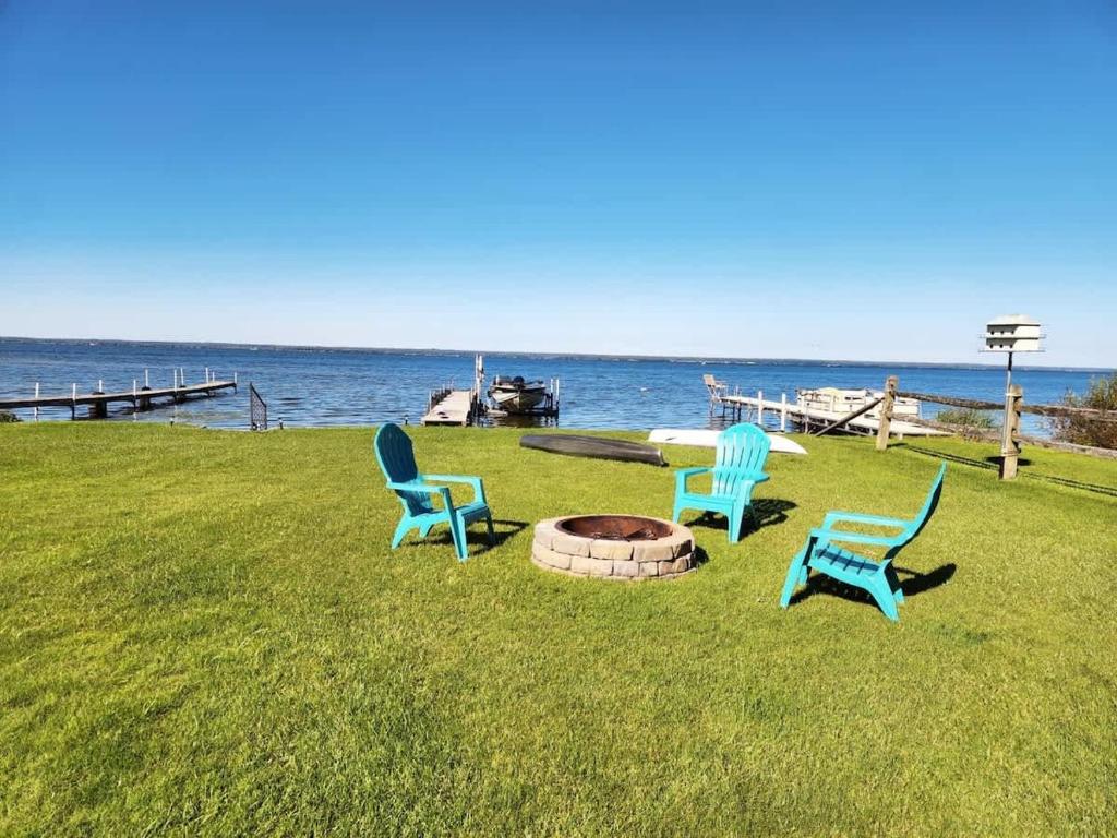 three chairs and a fire pit in the grass near the water at Oneida Lakeside Retreat in Bridgeport