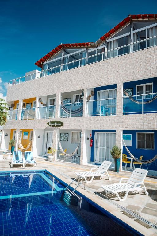 a hotel with a swimming pool and chairs and a building at Pequeno Paraíso Flats Praia Bela in Pitimbu