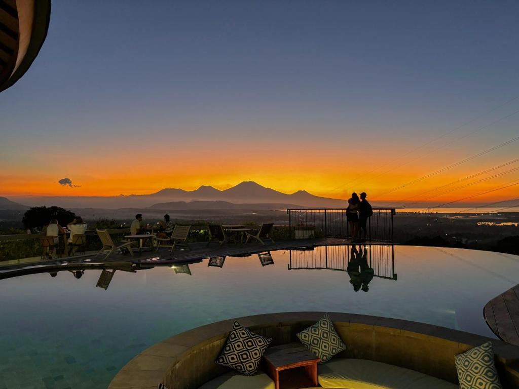 a sunset from a pool with people standing on the roof at Sumberkima Resort in Pemuteran