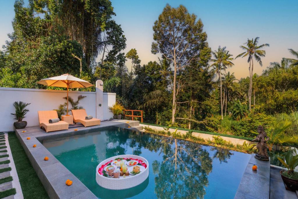an infinity pool with chairs and an umbrella next to a house at Rupa Arya Villa in Ubud