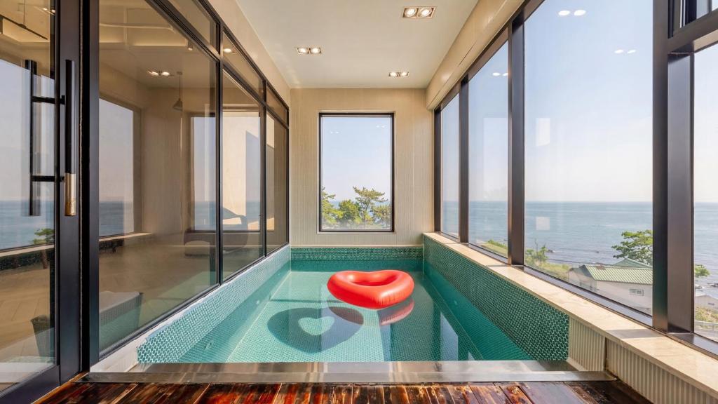 a swimming pool with a red chair in a room with windows at Pohang Sausalito by B-Class Pool Villa in Pohang