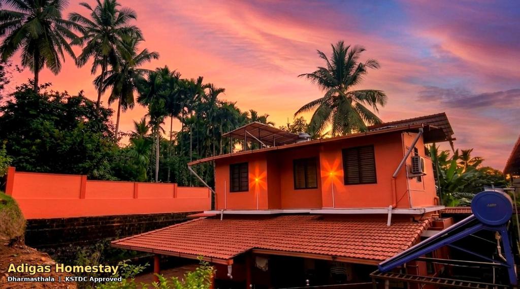 an orange house with palm trees in the background at Adiga's Homestay Dharmasthala in Dharmastala