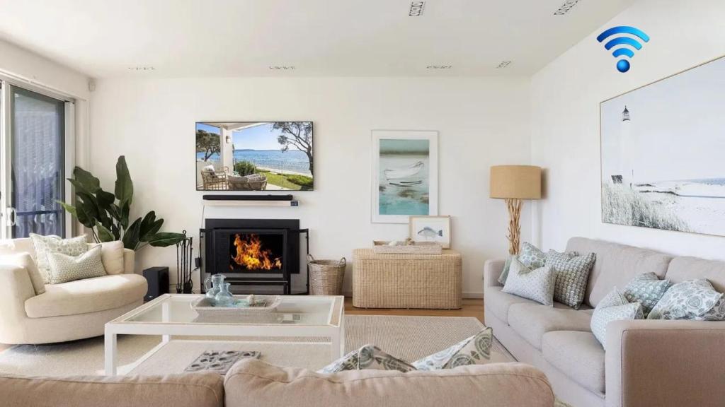 a living room with white furniture and a fireplace at Paradiso Beach House in Salamander Bay