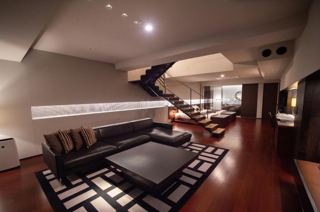a living room with a black leather couch and a staircase at Bourou Noguchi Hakodate in Hakodate