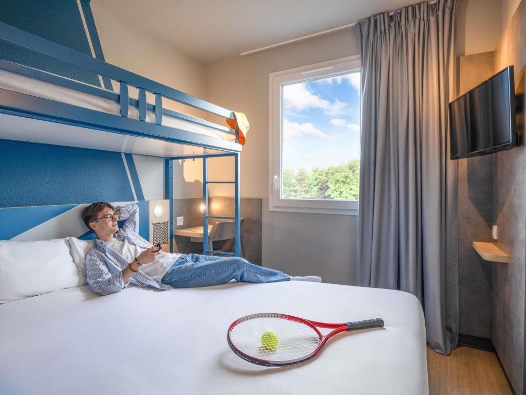 a woman laying on a bed with a tennis racket at Ibis Budget Orly Chevilly Tram 7 in Chevilly-Larue