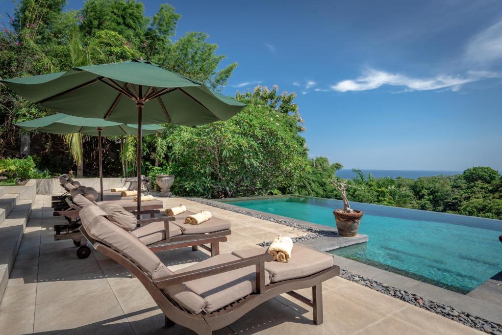 a group of lounge chairs with umbrellas next to a swimming pool at Villa Bayu - exclusive villa with infinity pool, wellness pavilion, panoramic ocean view & full service in Temukus
