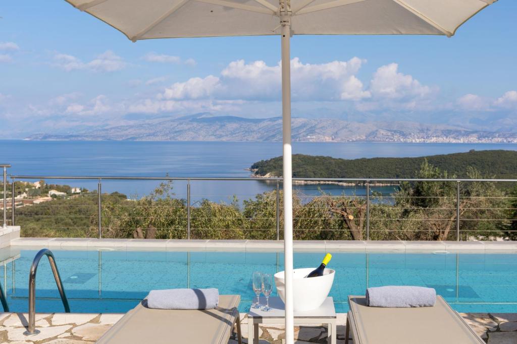 a swimming pool with an umbrella and a view of the water at Three Stones Villas by Rodostamo Collection in Kassiopi