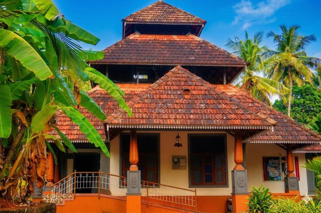 a building with a roof with palm trees in the background at Amma Stays and Trails in Kotikulam