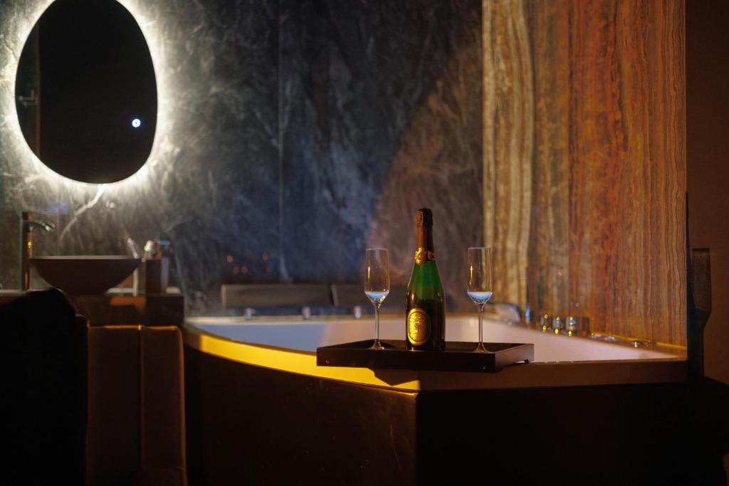 a bottle of champagne and two wine glasses on a bath tub at Suite Dark Luxe avec Écran géant de cinéma et jacuzzi in Clary