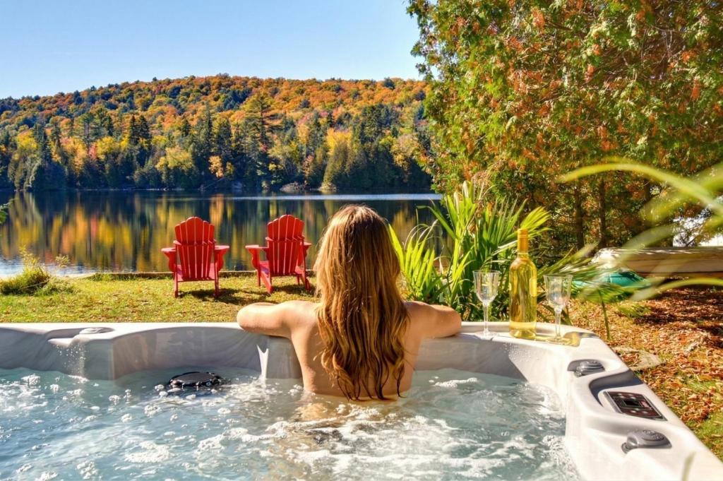 a woman sitting in a bath tub next to a lake at Bécassines Private Spa & Pool table , Waterfront in Nominingue