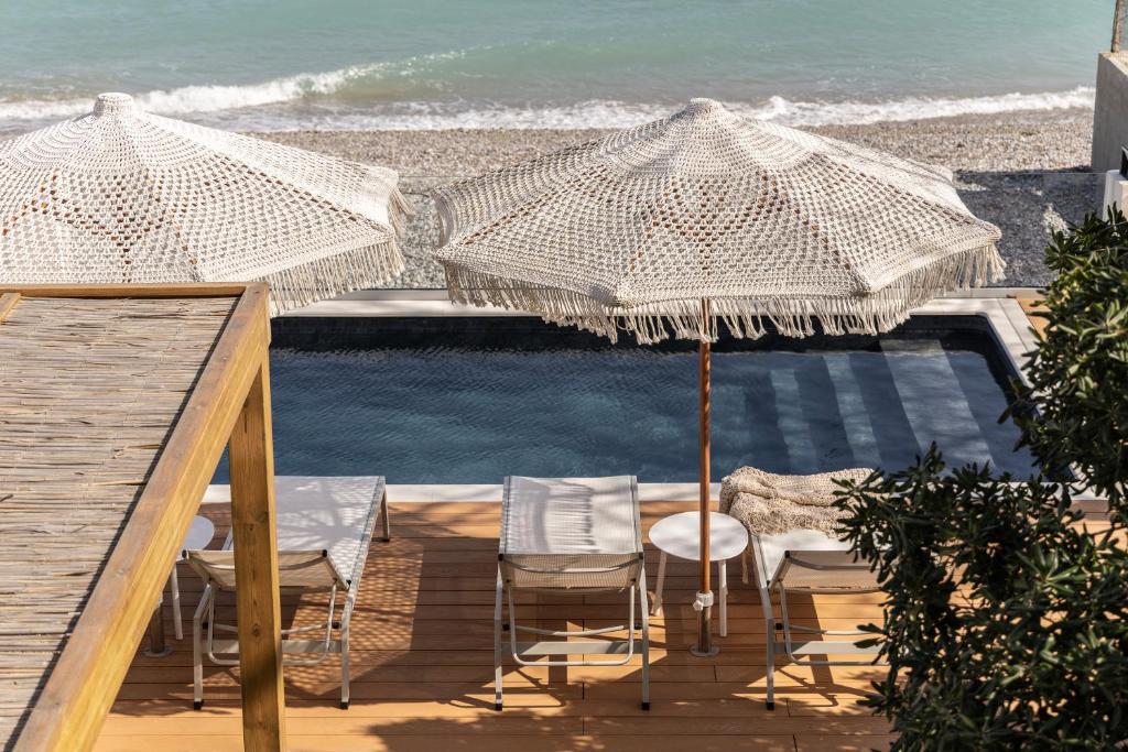 a deck with chairs and umbrellas next to a pool at Cavo Dio 1 - Beachfront bliss - Cozy Apt Pool Sunset in Káto Dhiminión