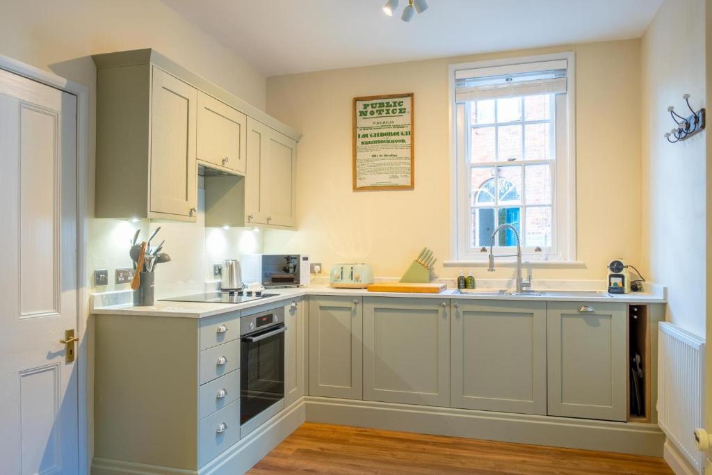 a kitchen with white cabinets and a sink and a window at Stable Yard Cottage in Osmaston