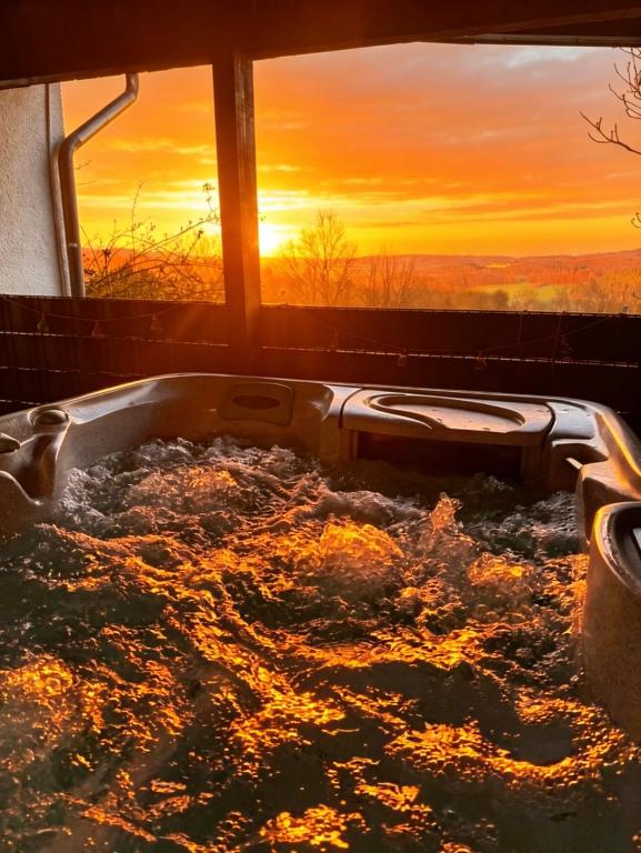 a bathtub filled with water with a sunset in the background at WW Luxury Cottage in Müschenbach