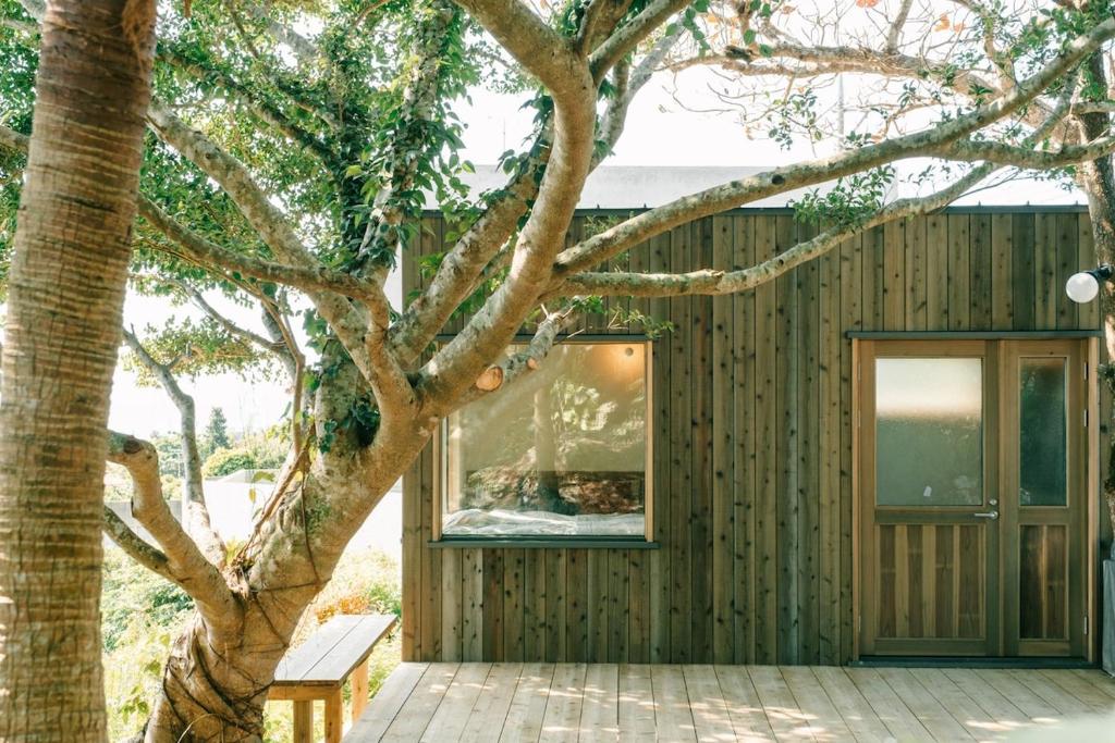 a wooden house with a tree in front of it at Ocean view cabin in Nanjo