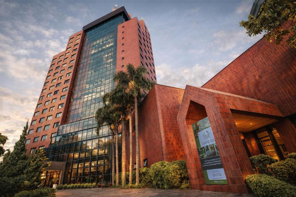 a tall brick building with a palm tree in front of it at Swan Novo Hamburgo in Novo Hamburgo