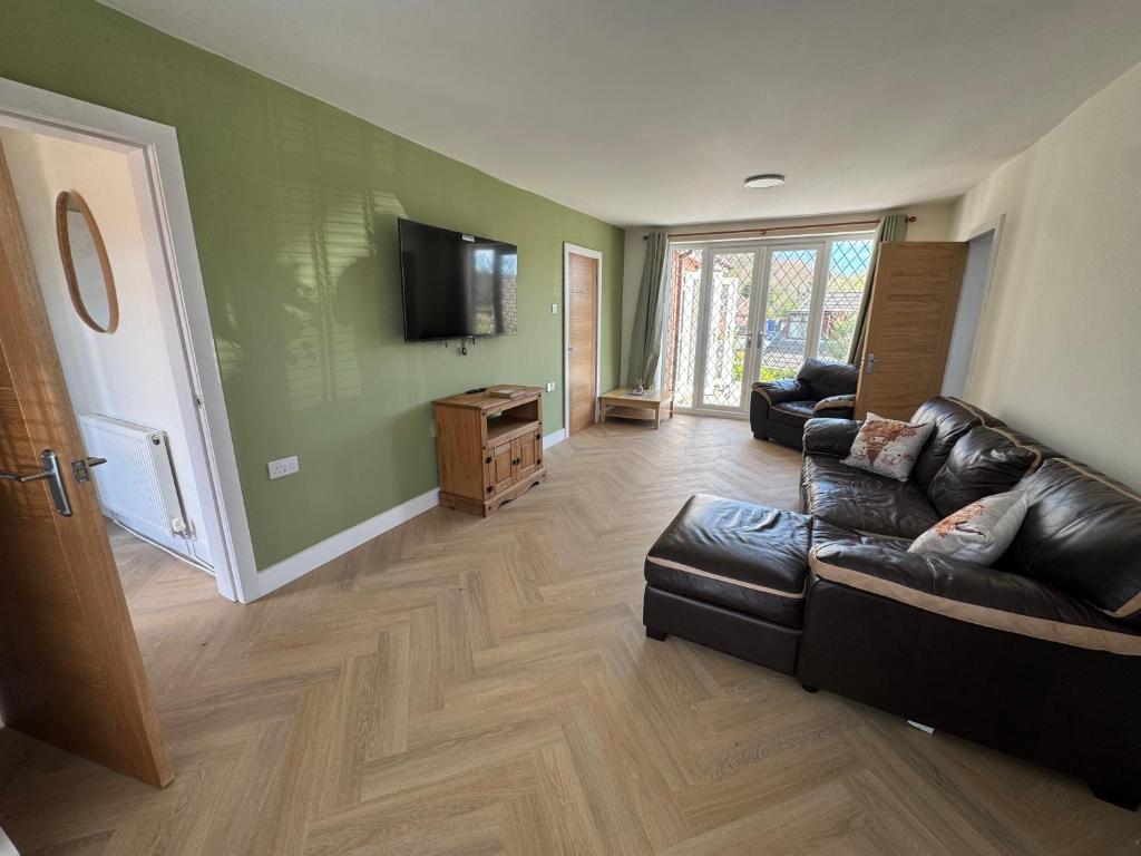 a living room with a leather couch and a tv at 2 Bedroom Bungalow by the Arches in Earlestown