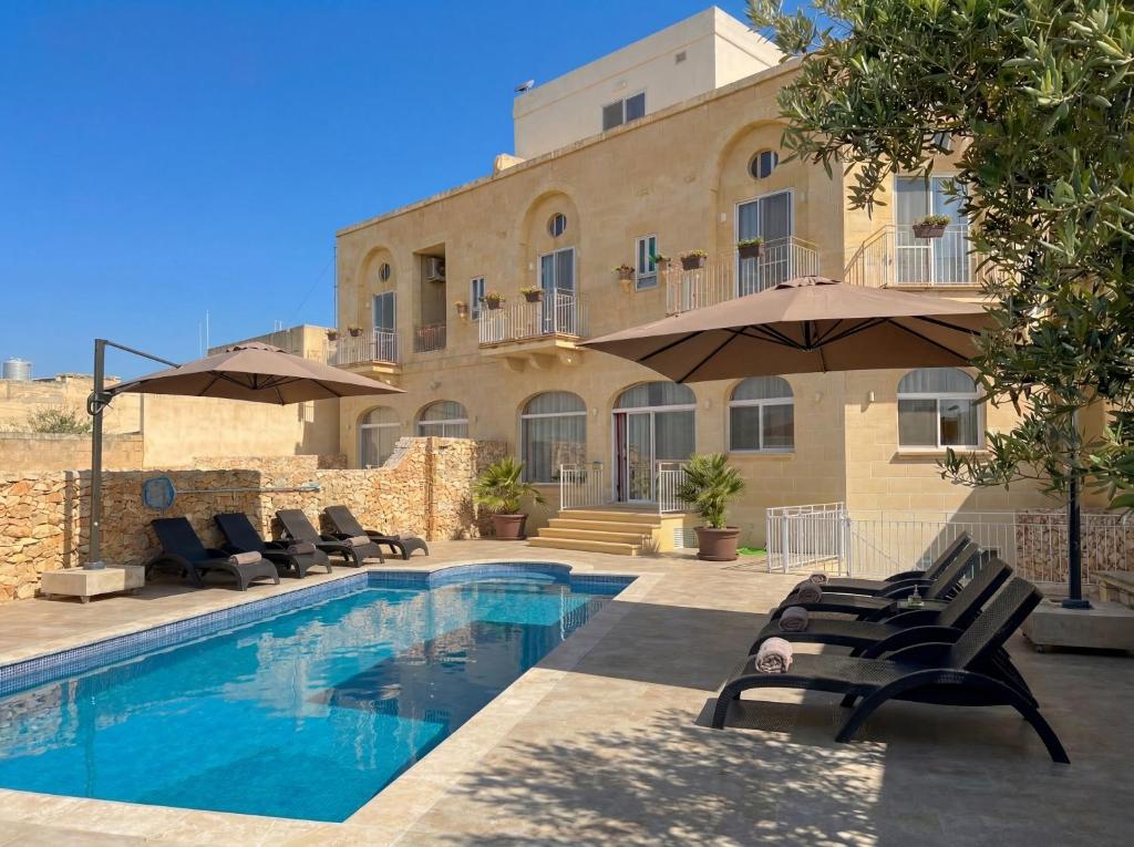 a pool with chairs and umbrellas in front of a building at Pitt House in Nadur