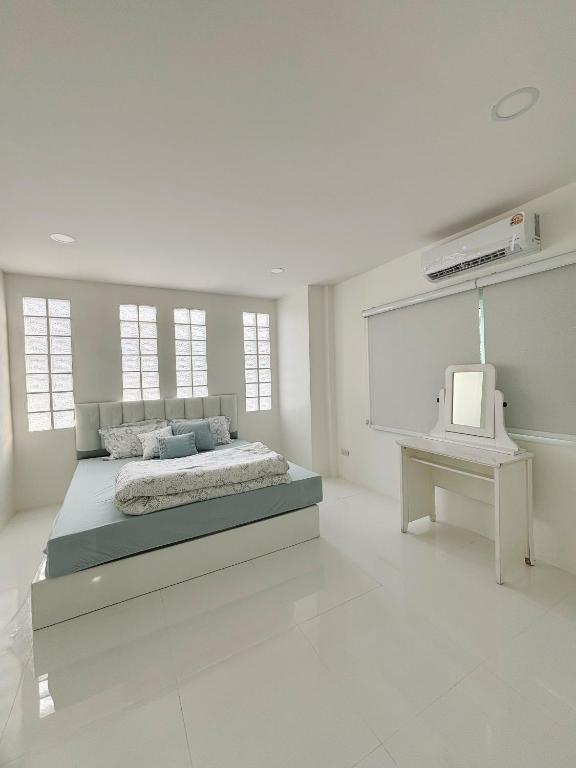 a white bedroom with a bed and a tv at Whitebeach Cottage in Chon Buri